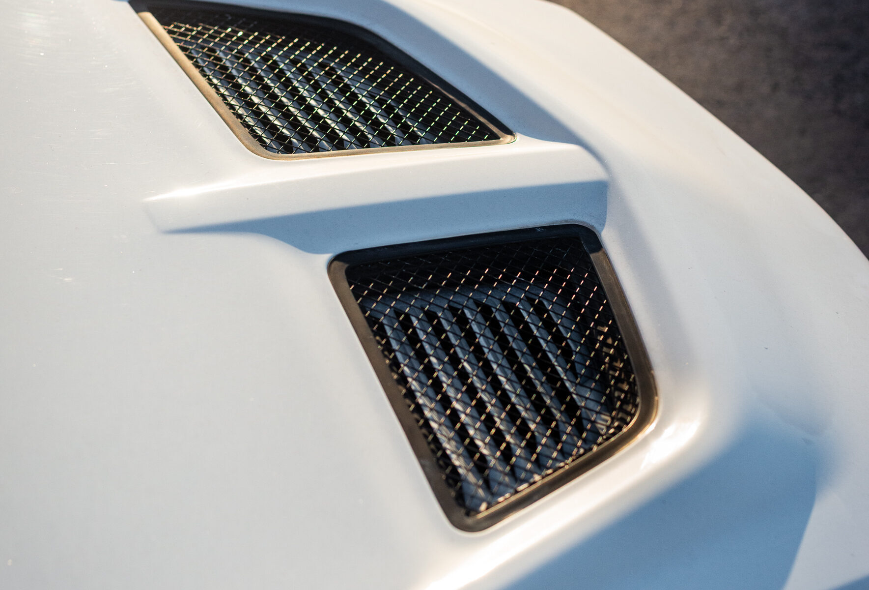 Close-up of a white car hood with two black mesh air vents.