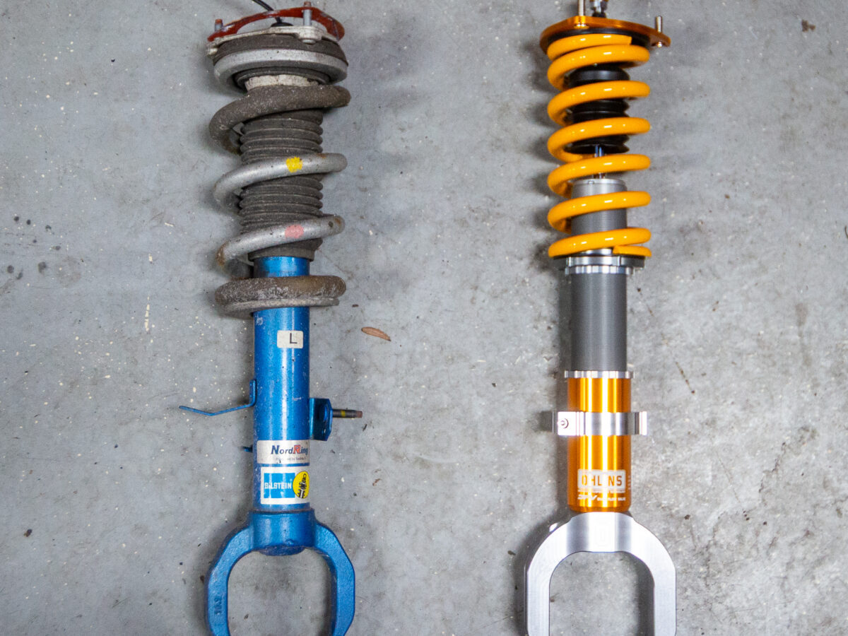 Old blue car suspension next to new yellow and silver suspension on concrete floor.