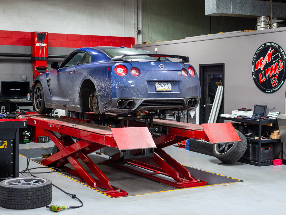Blue Nissan GT-R on a red hydraulic lift in a garage, surrounded by tools and equipment.