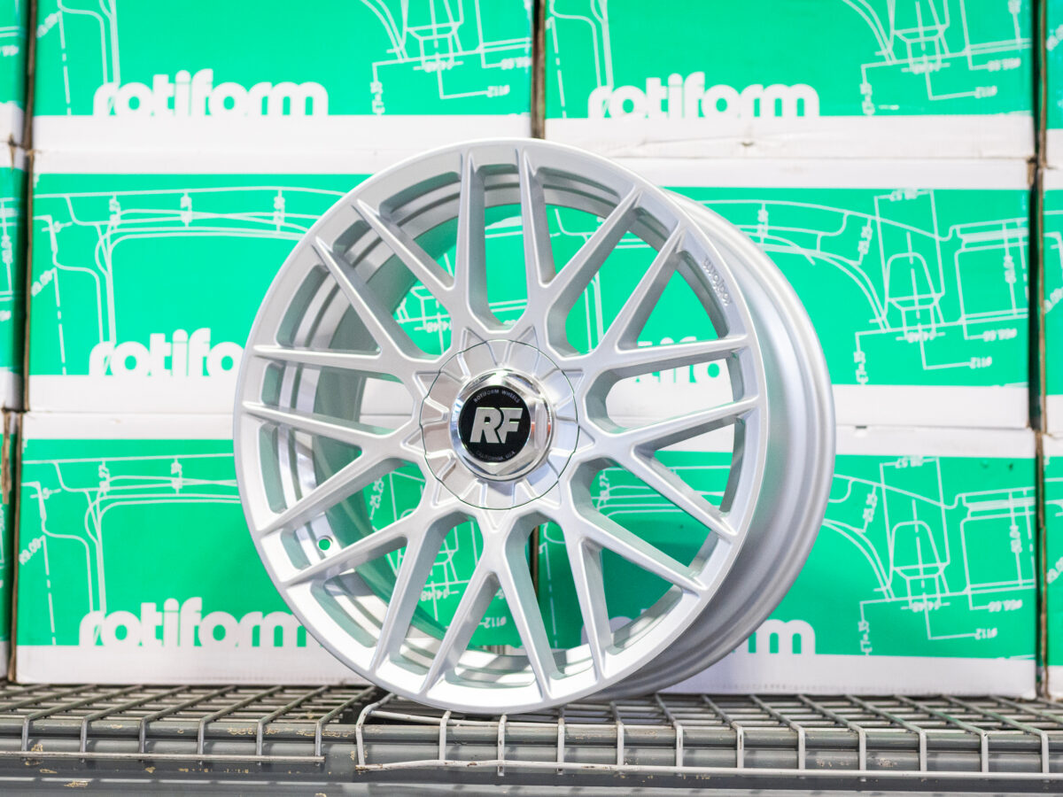 Silver alloy wheel with RF logo, displayed on a metal shelf, green Rotiform boxes in the background.