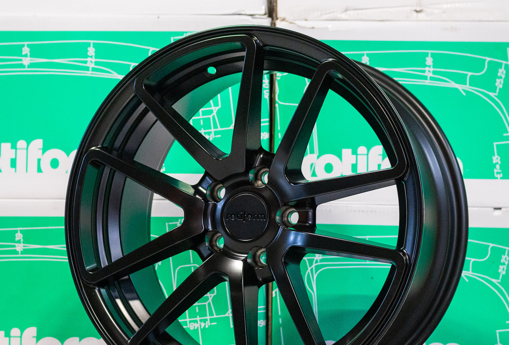 Black Rotiform wheel displayed against stacked green and white Rotiform boxes.
