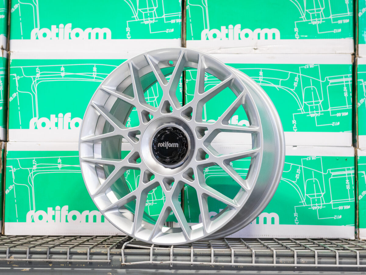 Silver Rotiform alloy wheel with intricate spoke design, displayed against green Rotiform boxes.