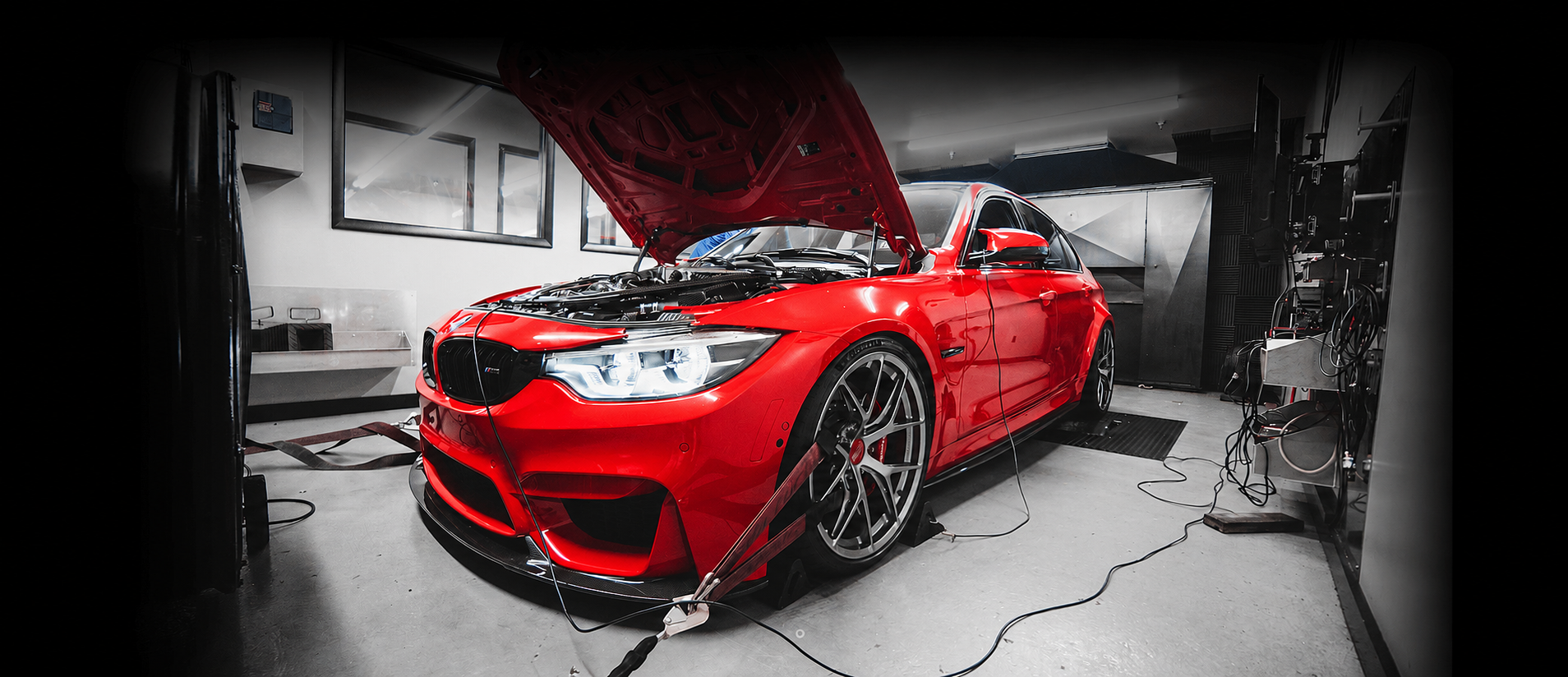 Red sports car with hood open, undergoing diagnostics in a garage, surrounded by equipment and cables.