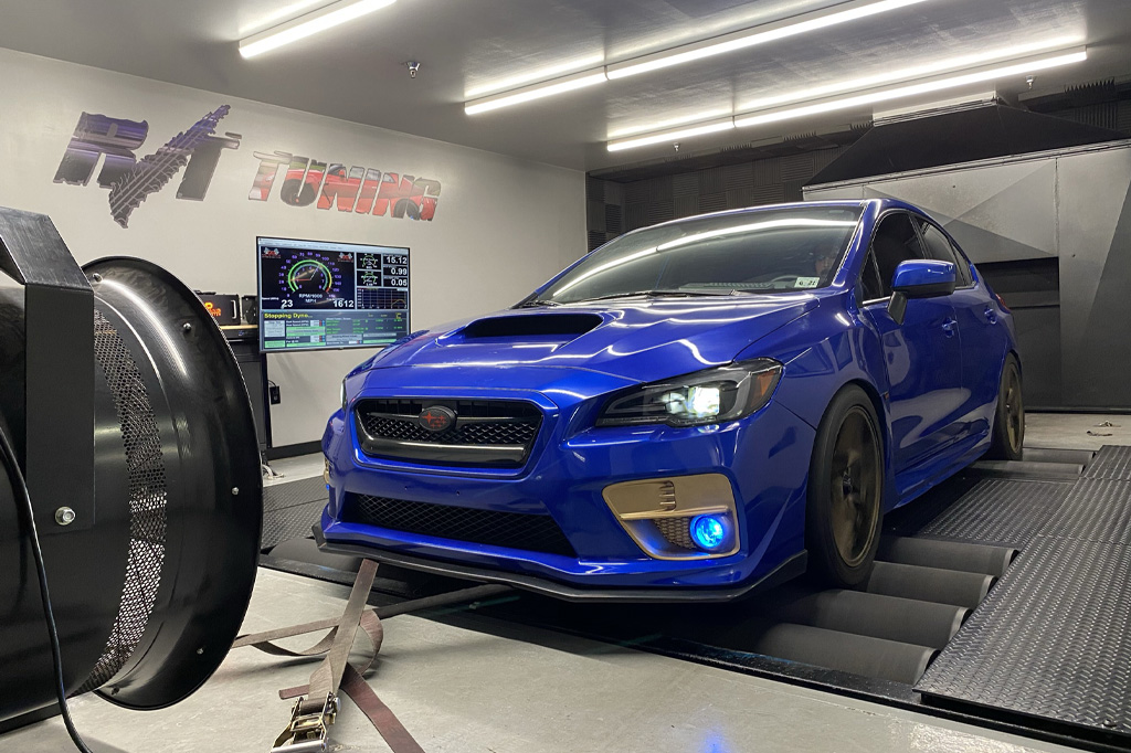 Blue car on a dynamometer in a tuning shop, with performance data displayed on a screen in the background.
