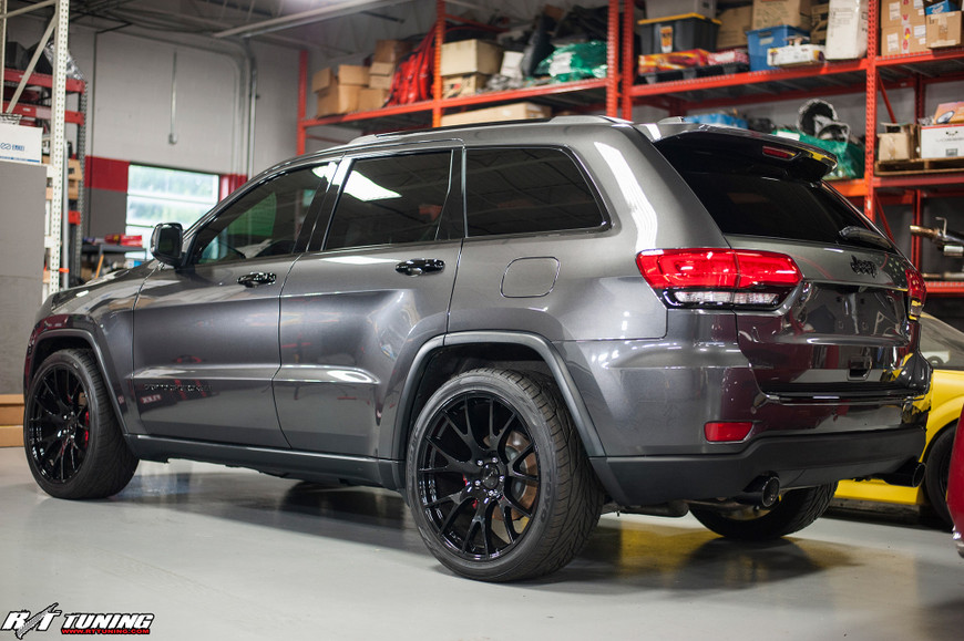 Gray Jeep Grand Cherokee with black rims in a garage, shelves with boxes in the background.