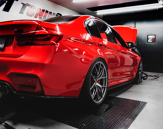 Red sports car on a dyno machine in a tuning garage, hood open, rear view.