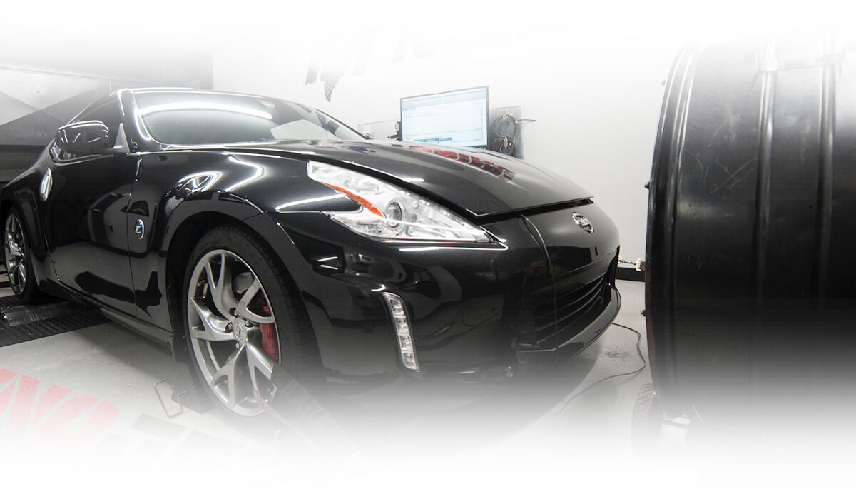 Black sports car on a dynamometer in a tuning garage, with a computer screen in the background.