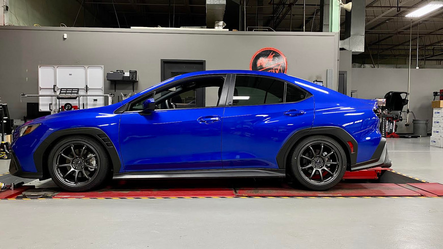 Blue 2022 Subaru WRX on a lift in a garage, side view, with black alloy wheels.