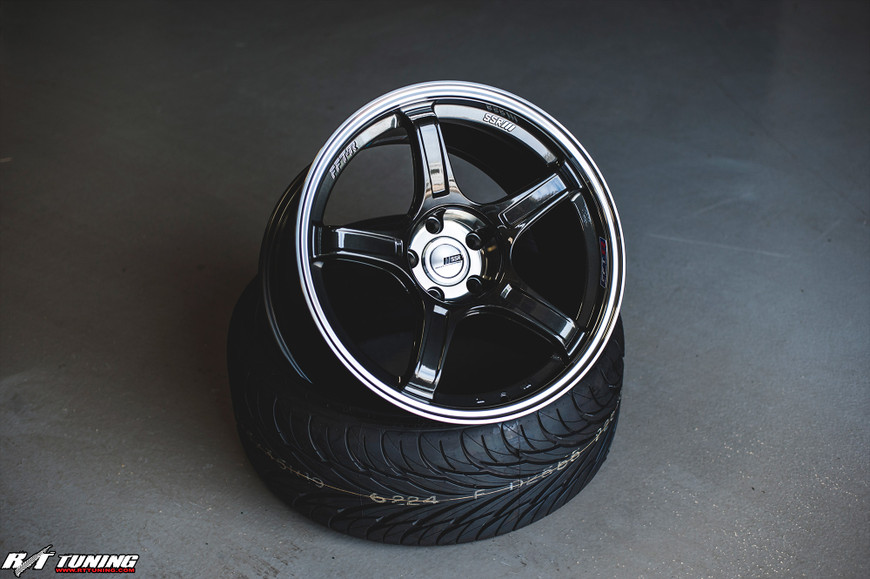 Black SSR GTX03 alloy wheel on top of two stacked tires in a garage setting.